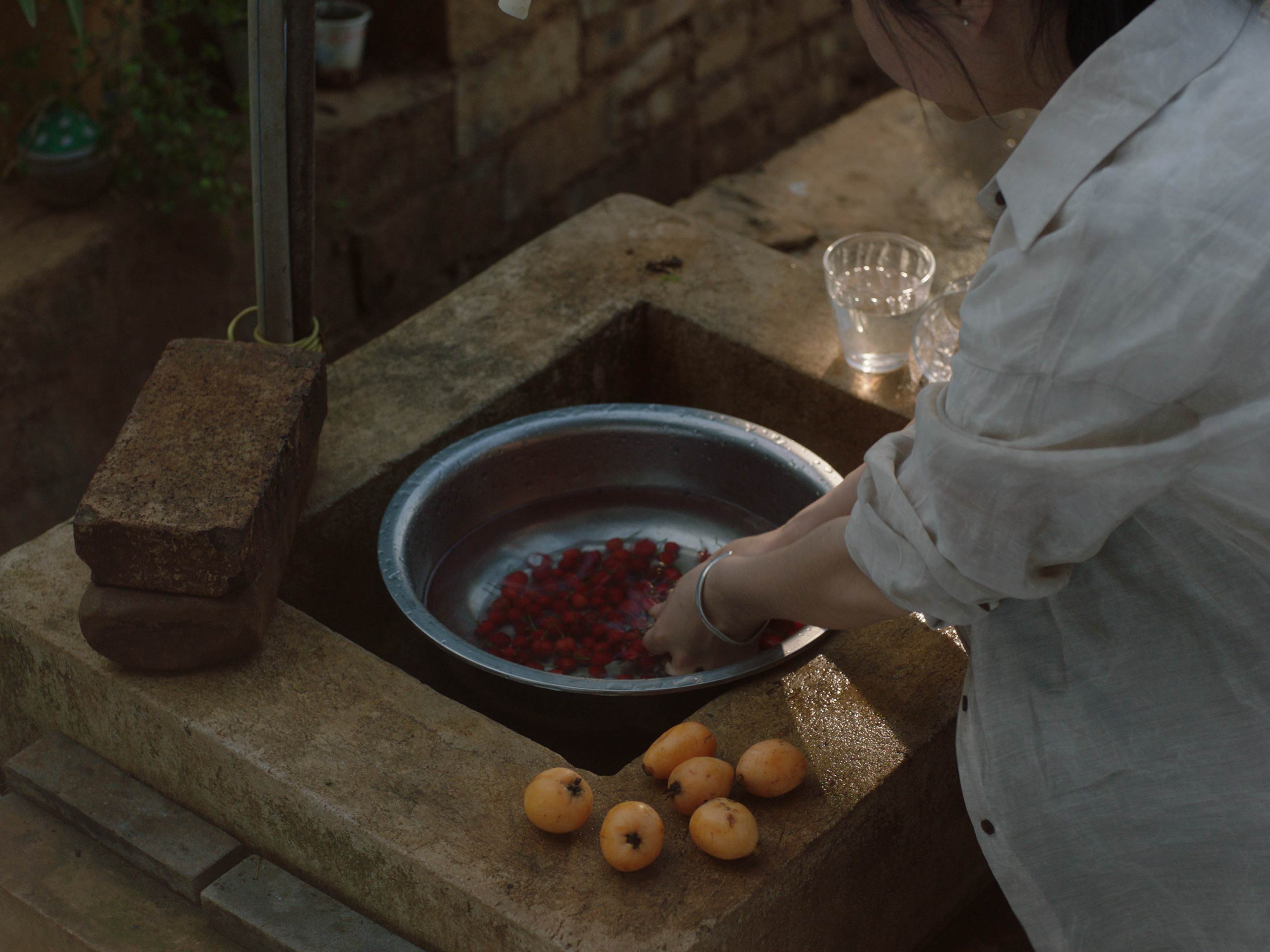 A still from A Silent Farewell: a woman washes fruit in a metal basin beside a stone sink.